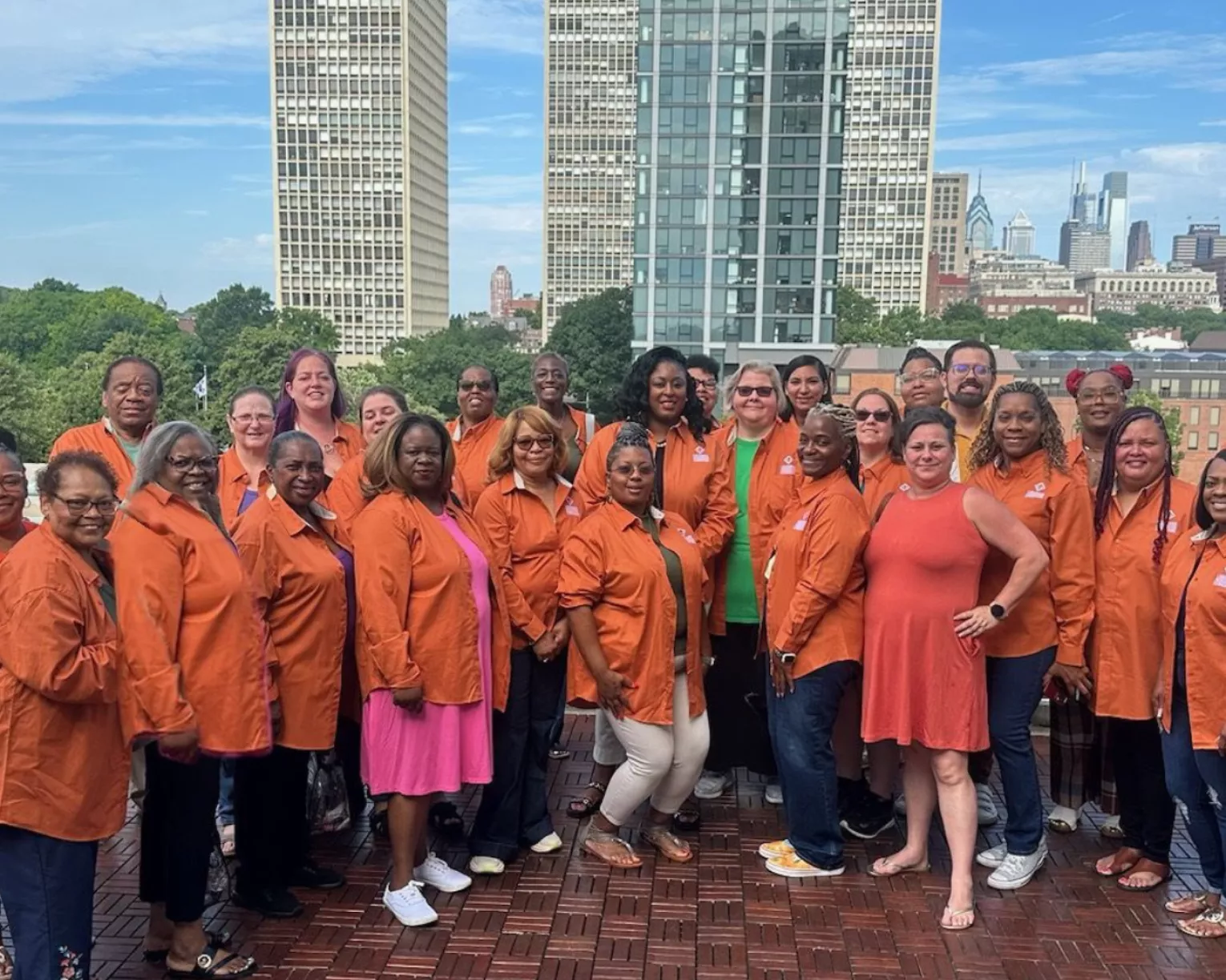 LAE member delegates wearing orange shirts pose for a picture on a city rooftop on a sunny day.