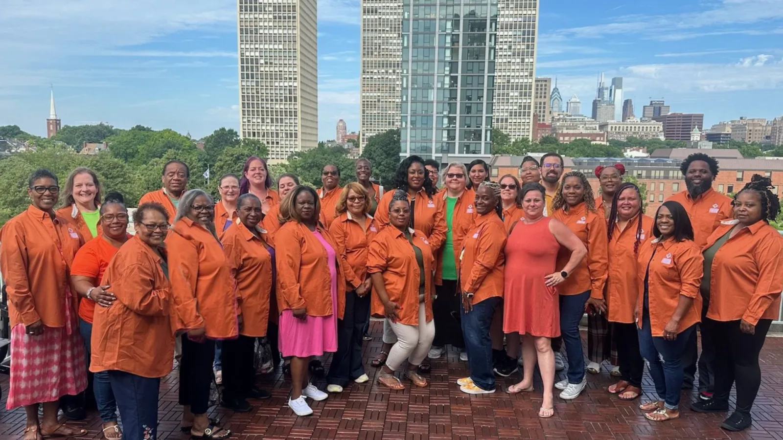 LAE member delegates wearing orange shirts pose for a picture on a city rooftop on a sunny day.